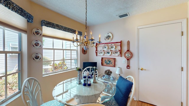 dining area featuring light hardwood / wood-style floors, a textured ceiling, and an inviting chandelier