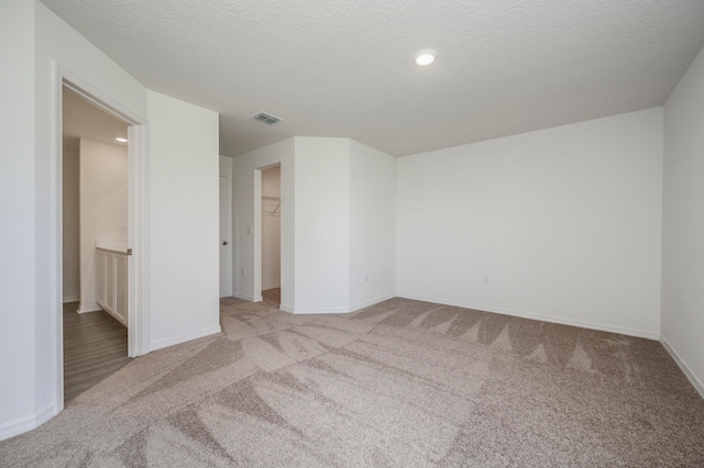 unfurnished bedroom with a textured ceiling, a walk in closet, light colored carpet, and a closet