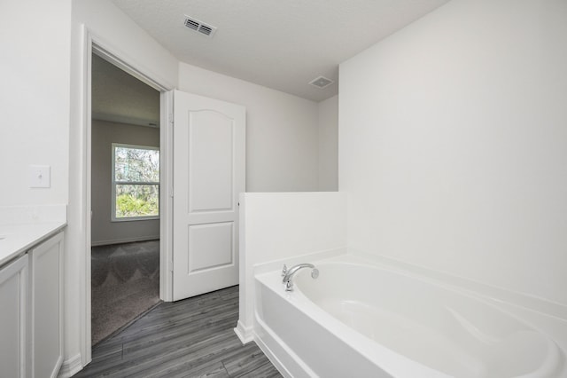 bathroom featuring hardwood / wood-style floors, vanity, a tub to relax in, and a textured ceiling