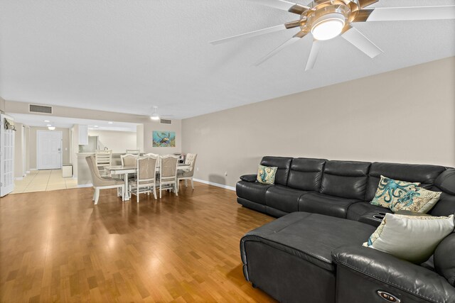 living room with light wood-style flooring, visible vents, ceiling fan, and baseboards