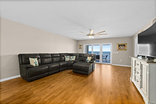 living area featuring light wood-type flooring, a textured ceiling, baseboards, and a ceiling fan