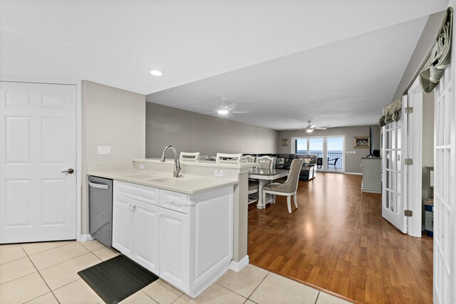 kitchen with light countertops, open floor plan, white cabinetry, a sink, and dishwasher