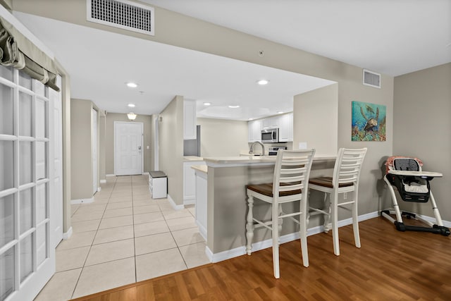 kitchen featuring kitchen peninsula, a breakfast bar, light hardwood / wood-style flooring, and white cabinetry