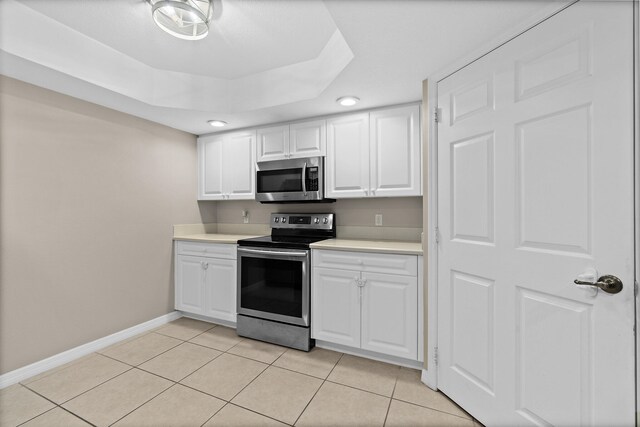 kitchen featuring white cabinets, appliances with stainless steel finishes, a tray ceiling, light countertops, and light tile patterned flooring