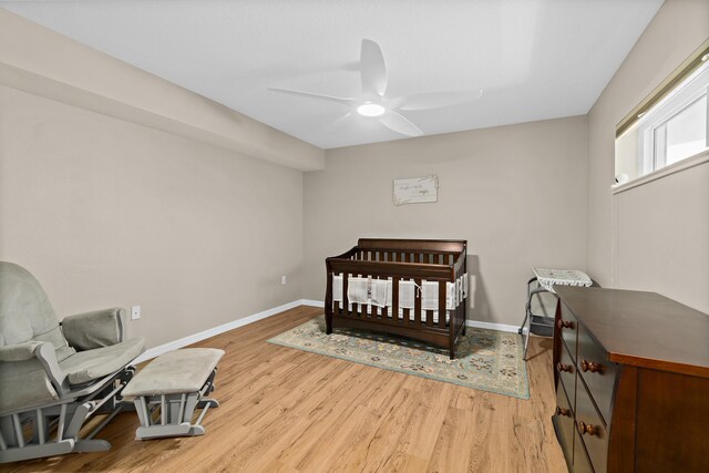 bedroom with a ceiling fan, a nursery area, light wood-style flooring, and baseboards