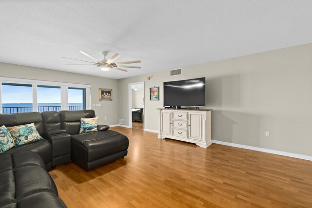 living room featuring a water view, visible vents, ceiling fan, wood finished floors, and baseboards