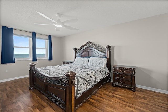 bedroom featuring a water view, dark wood finished floors, and baseboards