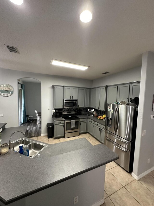 kitchen with kitchen peninsula, stainless steel appliances, light tile floors, gray cabinetry, and sink