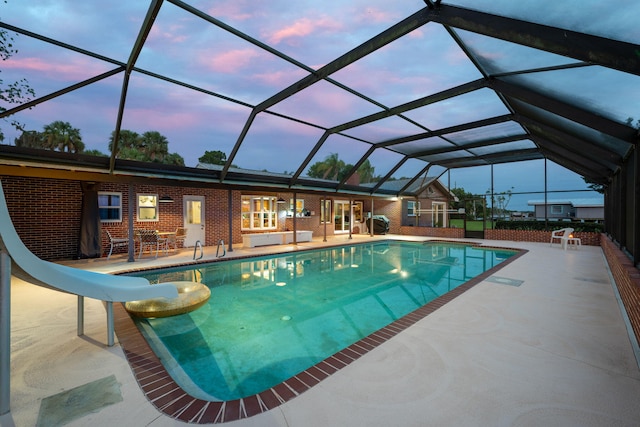 pool at dusk featuring a water slide, a patio, and a lanai