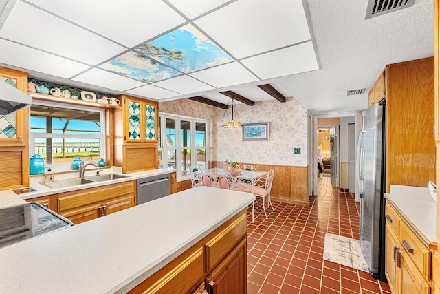 kitchen with pendant lighting, appliances with stainless steel finishes, sink, and wood walls