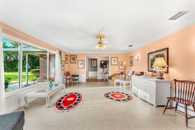 living area featuring crown molding, ceiling fan, and a textured ceiling