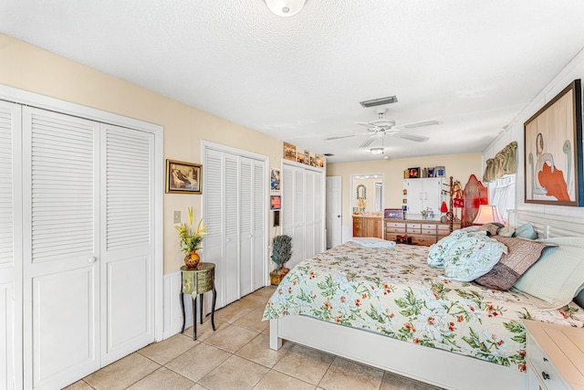 tiled bedroom featuring ceiling fan, a textured ceiling, and two closets