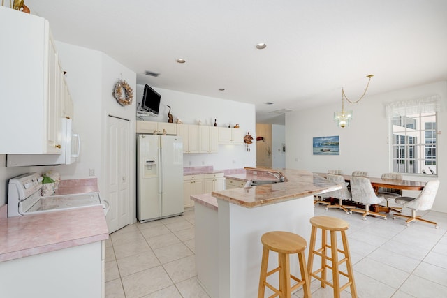 kitchen with stove, sink, white fridge with ice dispenser, a notable chandelier, and a breakfast bar area