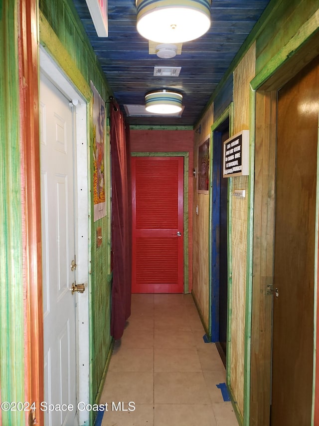 hall featuring light tile patterned floors and wood walls