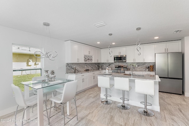 kitchen featuring light stone countertops, stainless steel appliances, sink, white cabinets, and hanging light fixtures