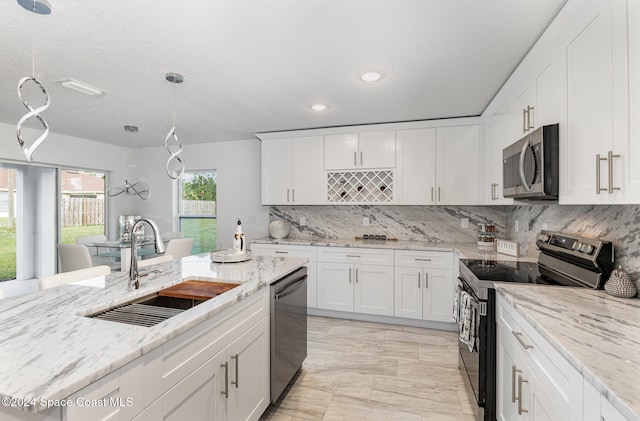 kitchen with light stone counters, stainless steel appliances, sink, decorative light fixtures, and white cabinets