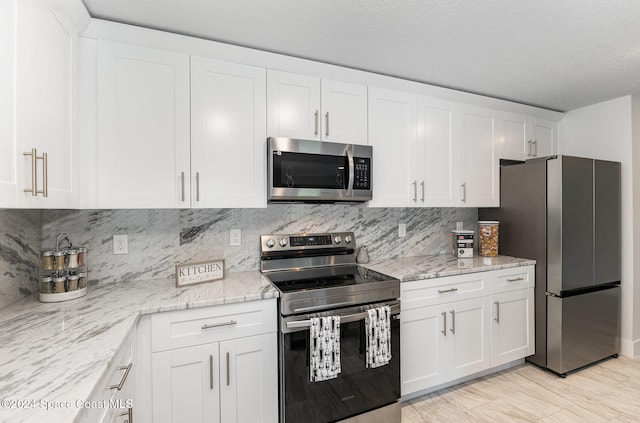 kitchen with stainless steel appliances, white cabinetry, and light stone counters