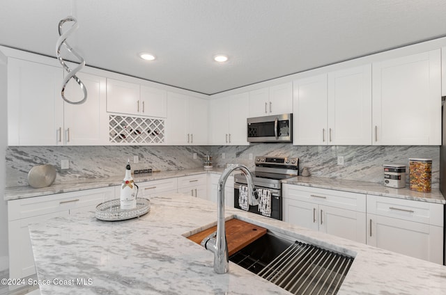 kitchen featuring tasteful backsplash, light stone counters, stainless steel appliances, sink, and white cabinetry