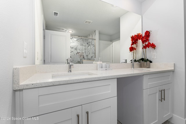 bathroom with a textured ceiling, vanity, and a shower with shower door