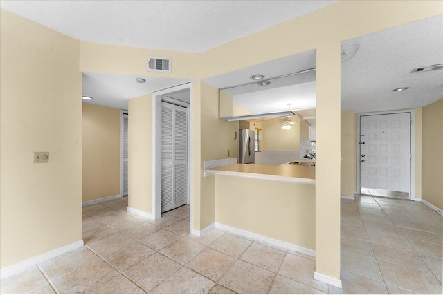 kitchen with stainless steel fridge, sink, light tile patterned floors, and a textured ceiling