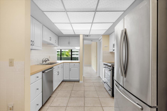 kitchen featuring sink, stainless steel appliances, tasteful backsplash, a paneled ceiling, and white cabinets