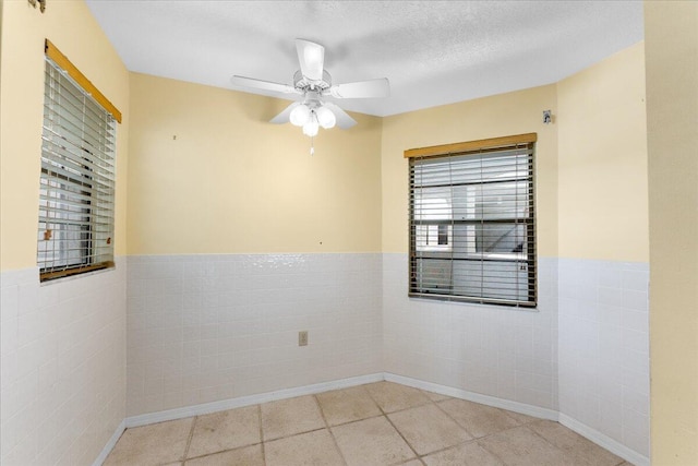 unfurnished room with a textured ceiling, ceiling fan, and tile walls