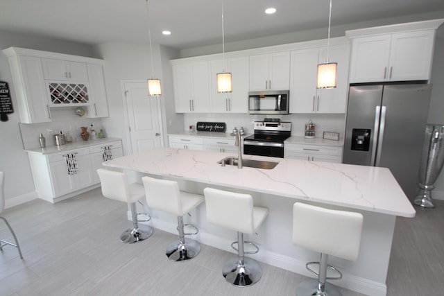 kitchen with a kitchen island with sink, hanging light fixtures, white cabinetry, a breakfast bar area, and stainless steel appliances