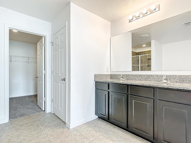 bathroom featuring tile patterned floors, vanity, a shower with door, and a textured ceiling