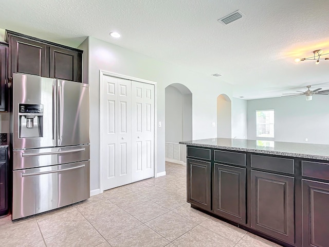 kitchen featuring dark brown cabinetry, stainless steel fridge with ice dispenser, light tile patterned floors, and stone countertops