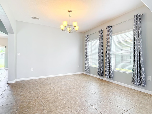 tiled empty room with plenty of natural light and a chandelier