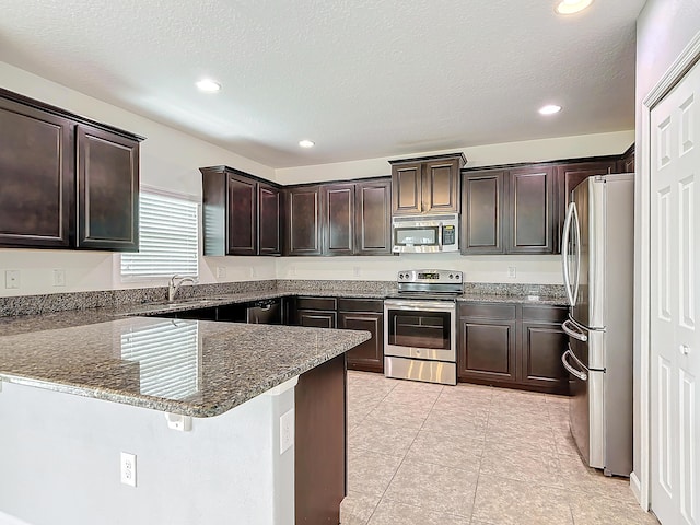 kitchen featuring stone counters, appliances with stainless steel finishes, dark brown cabinetry, a kitchen bar, and kitchen peninsula