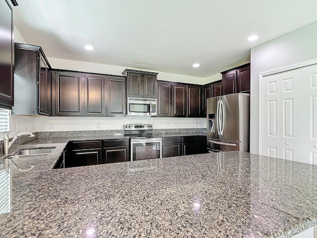 kitchen with sink, dark stone countertops, kitchen peninsula, stainless steel appliances, and dark brown cabinets