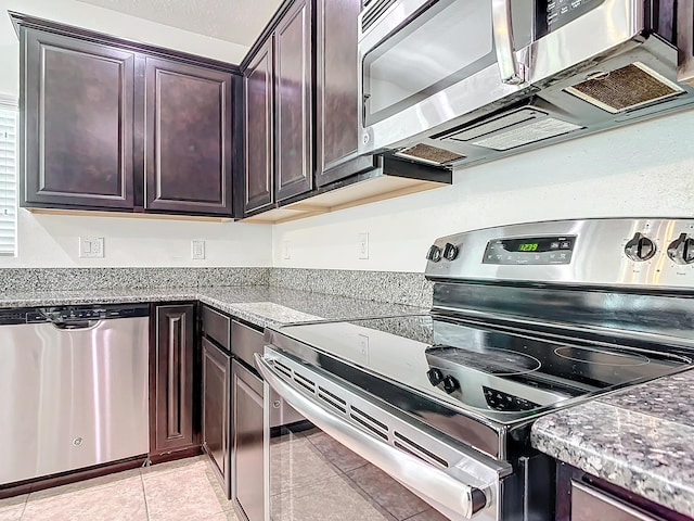 kitchen with stone counters, appliances with stainless steel finishes, light tile patterned floors, and dark brown cabinetry