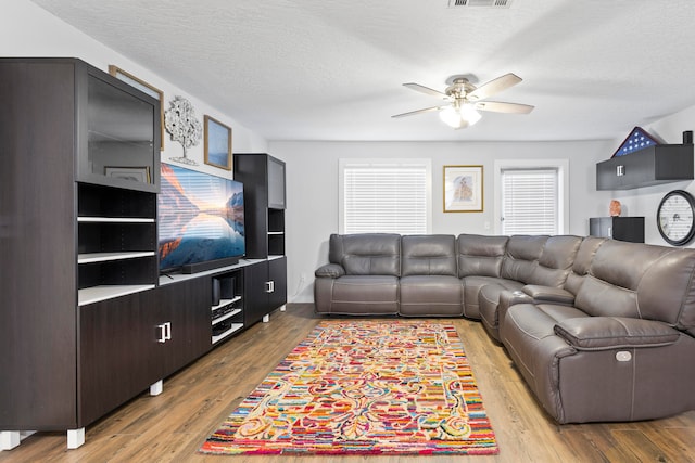 living room with a textured ceiling, hardwood / wood-style flooring, and ceiling fan