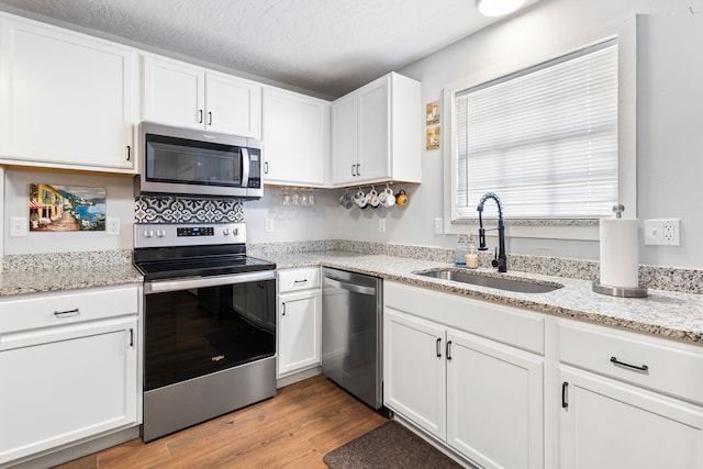 kitchen with light stone counters, stainless steel appliances, sink, light hardwood / wood-style flooring, and white cabinetry