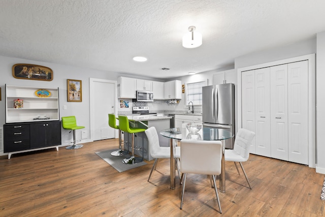 dining area with sink, wood-type flooring, and a textured ceiling