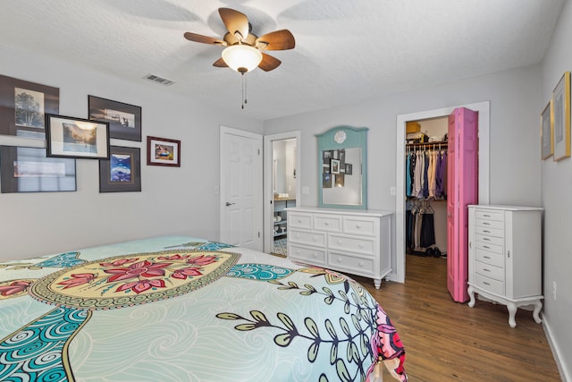 bedroom with a walk in closet, ceiling fan, a textured ceiling, dark hardwood / wood-style flooring, and a closet