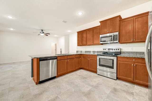 kitchen featuring sink, stone countertops, a textured ceiling, kitchen peninsula, and stainless steel appliances