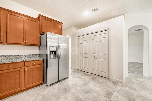 kitchen featuring stainless steel refrigerator with ice dispenser, light stone counters, and a textured ceiling