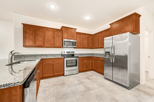 kitchen featuring appliances with stainless steel finishes, light stone countertops, sink, and a textured ceiling