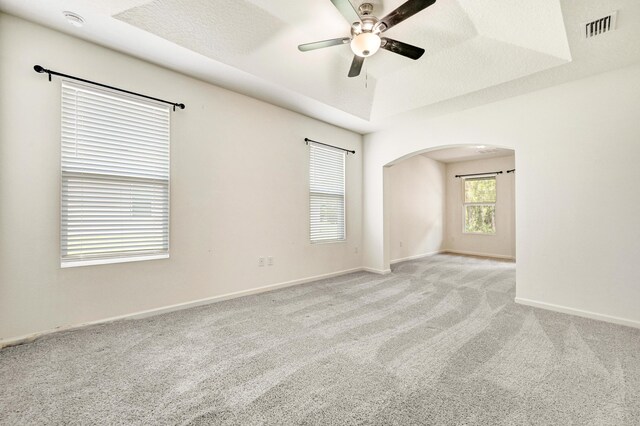 carpeted empty room with a textured ceiling, a raised ceiling, and ceiling fan