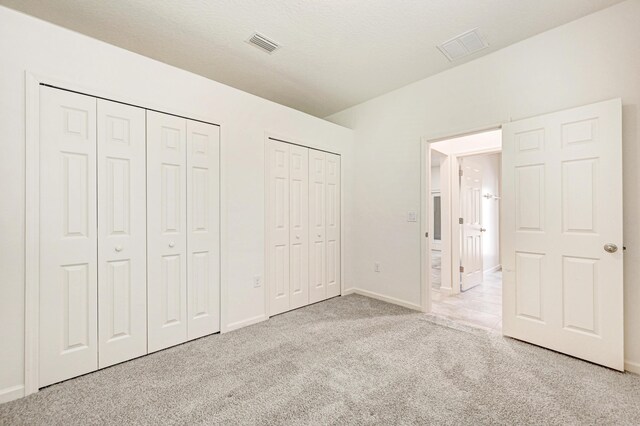 unfurnished bedroom with light carpet and two closets