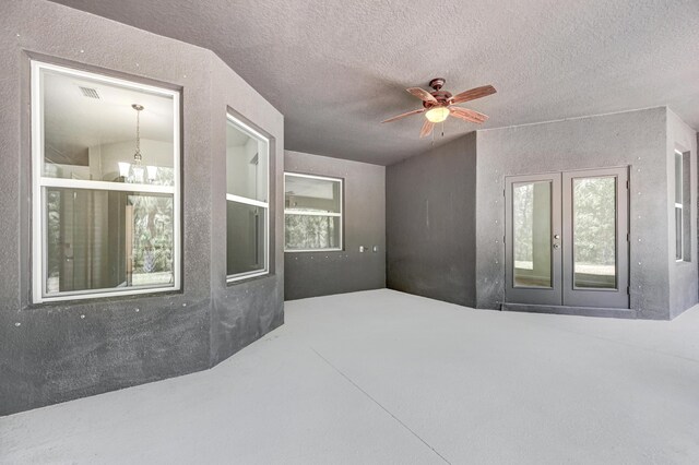 interior space with ceiling fan with notable chandelier, a textured ceiling, and french doors