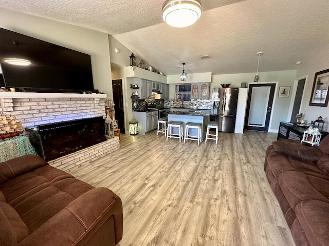 living room featuring light hardwood / wood-style flooring, vaulted ceiling, a textured ceiling, and a brick fireplace