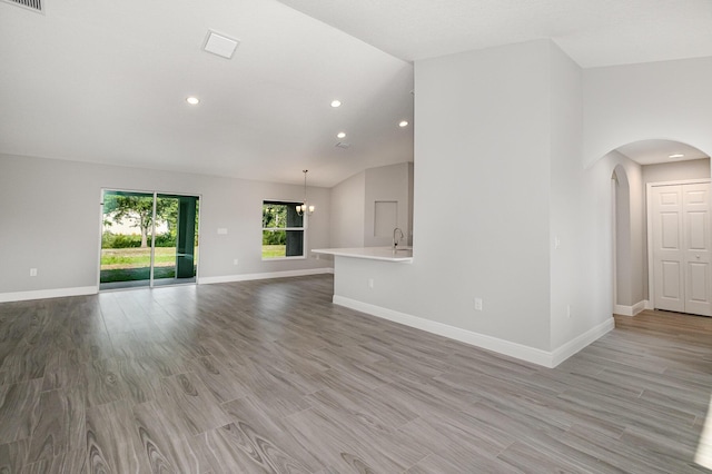 unfurnished living room featuring sink, light hardwood / wood-style flooring, lofted ceiling, and an inviting chandelier