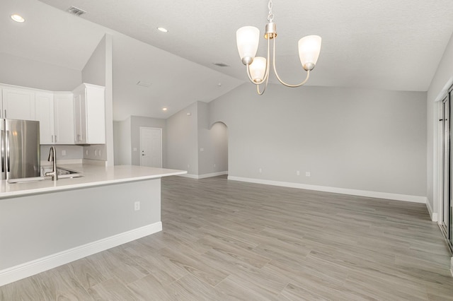 kitchen with pendant lighting, stainless steel fridge, white cabinetry, vaulted ceiling, and a chandelier