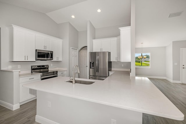 kitchen featuring sink, stainless steel appliances, kitchen peninsula, vaulted ceiling, and white cabinets