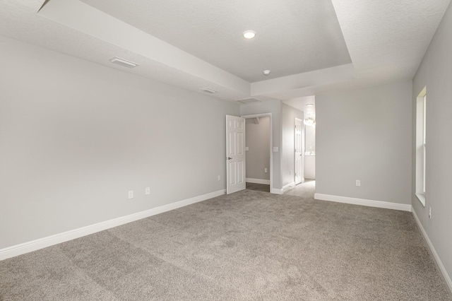 unfurnished bedroom with ensuite bathroom, a tray ceiling, carpet floors, and a textured ceiling