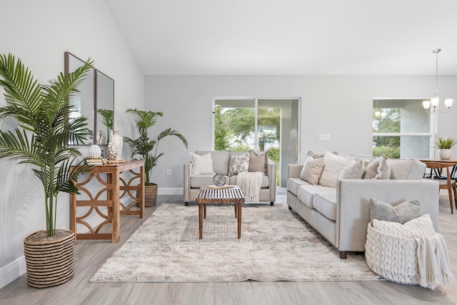 living room with a chandelier, light hardwood / wood-style floors, vaulted ceiling, and a healthy amount of sunlight