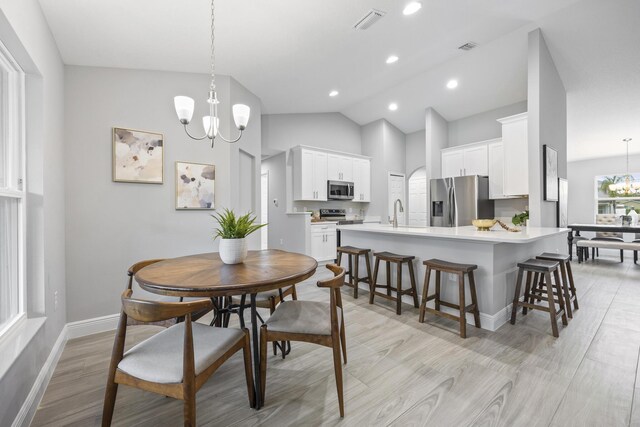 dining area featuring light hardwood / wood-style floors, lofted ceiling, and a notable chandelier